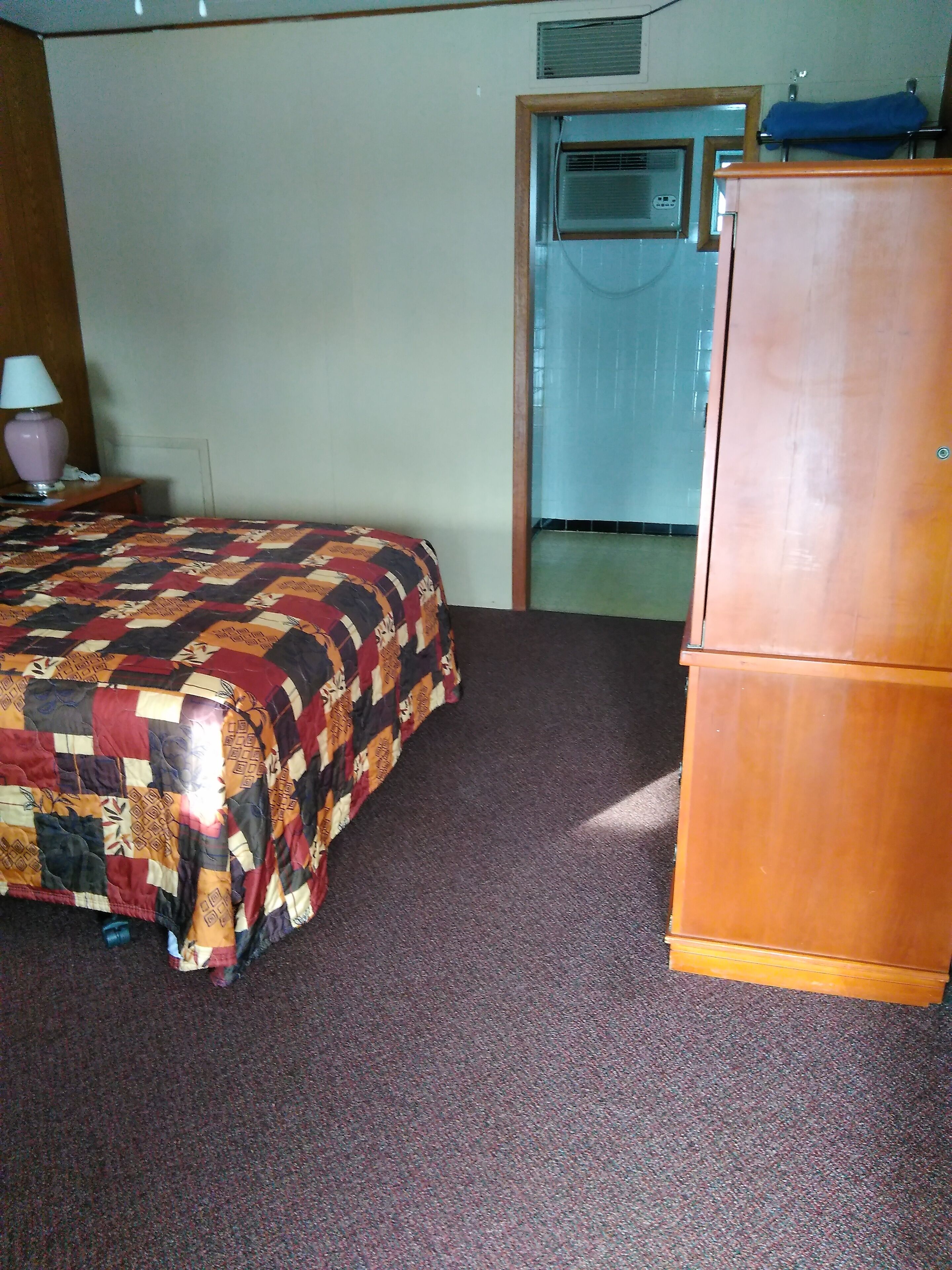 Une chambre à coucher comprenant un lit, une commode, une table de chevet, une lampe et un appareil de climatisation.