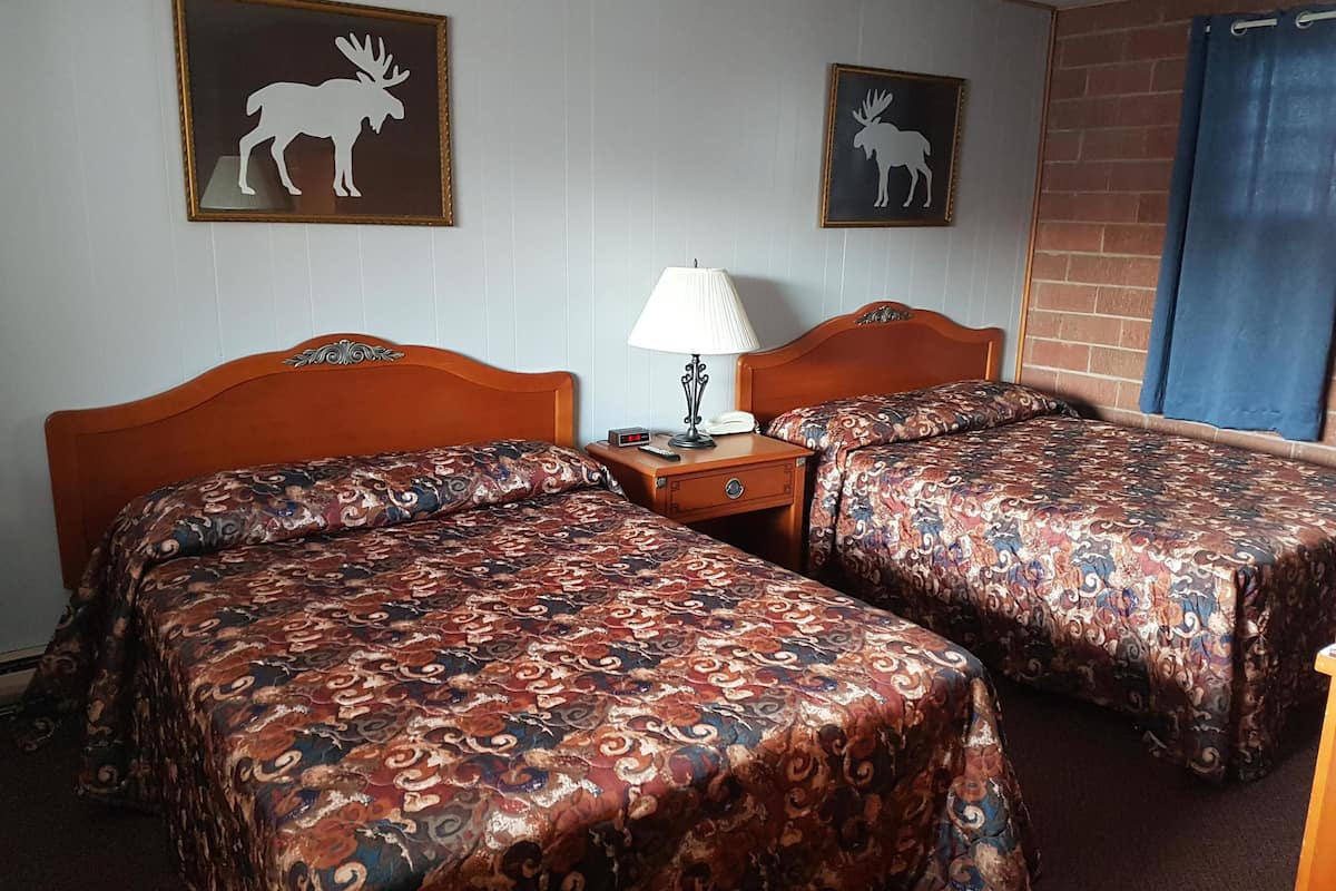 A hotel room with two wooden beds, a nightstand with a lamp, and two moose-themed wall art pieces.