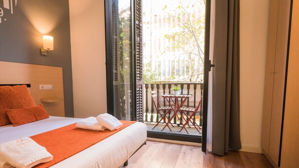 Ein Hotelzimmer mit Bett, einem Balkon mit Tisch und Stühlen und Blick auf die Stadt.
