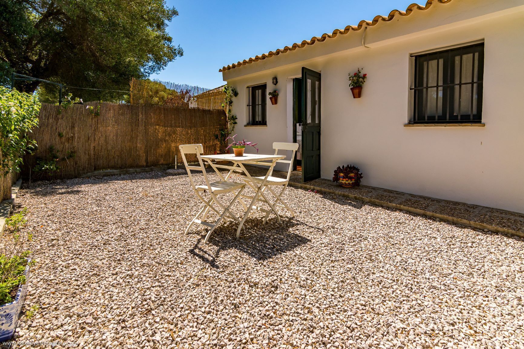 Eine Terrasse mit Tisch und Stühlen, ein Holzzaun und ein Gebäude mit Ziegeldach.