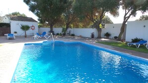 A rectangular swimming pool with clear blue water, surrounded by a white wall and a grassy area. There are two lounge chairs and a table with chairs. - Cortijo el Indiviso (Barbate)