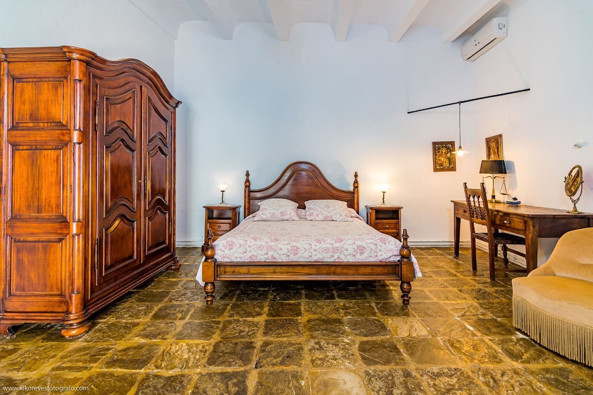 A bedroom with a wooden bed, a wardrobe, a desk, and a chair.