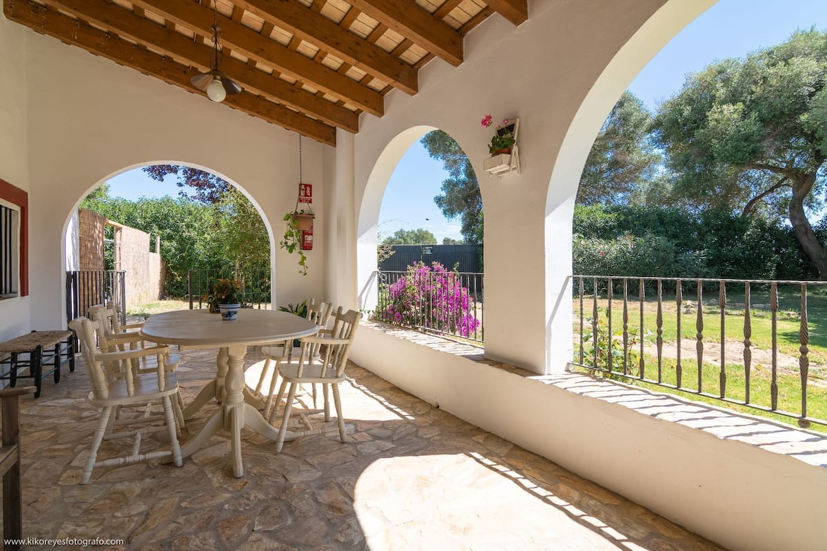 An outdoor patio with a round table and chairs, surrounded by stone flooring and white walls.