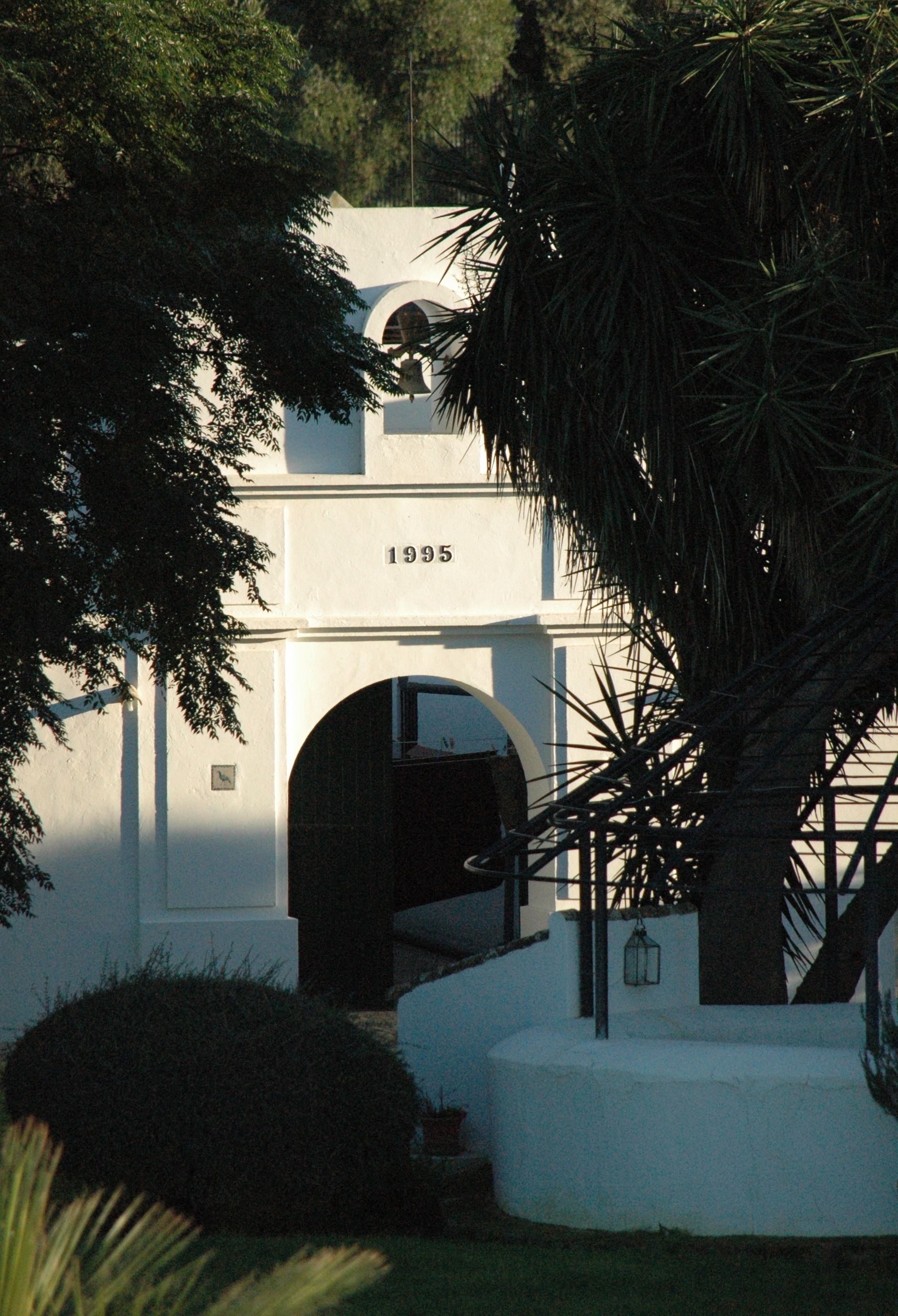 Un edificio con fachada blanca, un amplio arco de entrada y el año '1995' exhibido sobre la entrada.