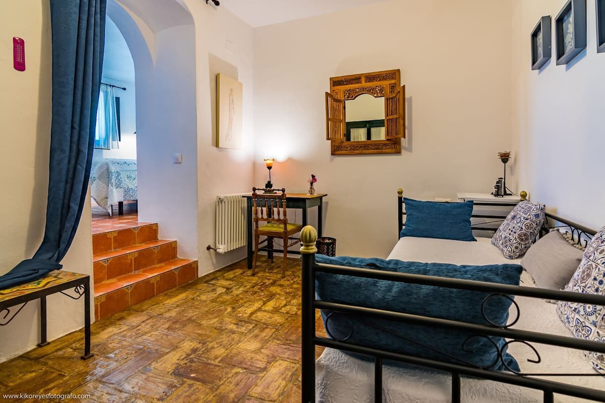 A bedroom with a bed, a chair, a table, a mirror, and a staircase leading to another room.