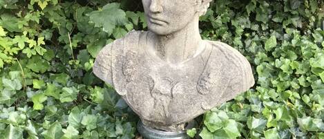 A stone bust sculpture surrounded by dense green foliage.