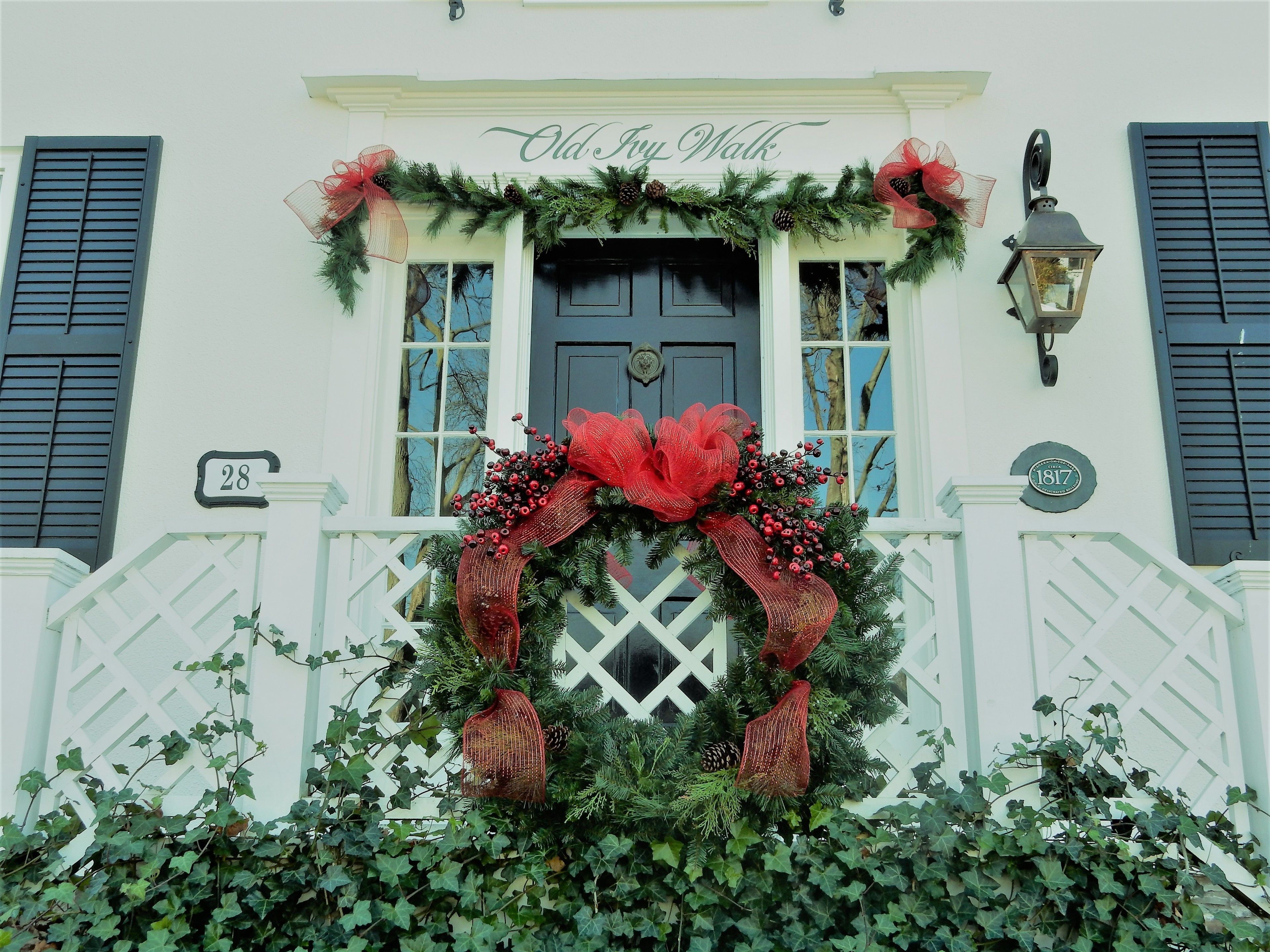 A building with a white facade, black shutters, and a black door. A large red bow and greenery adorn the entrance.