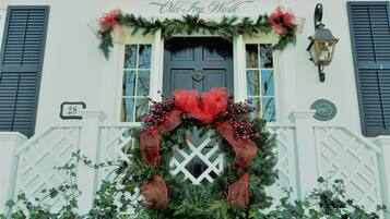 A building with a white facade, black shutters, and a black door. A large red bow and greenery adorn the entrance.
