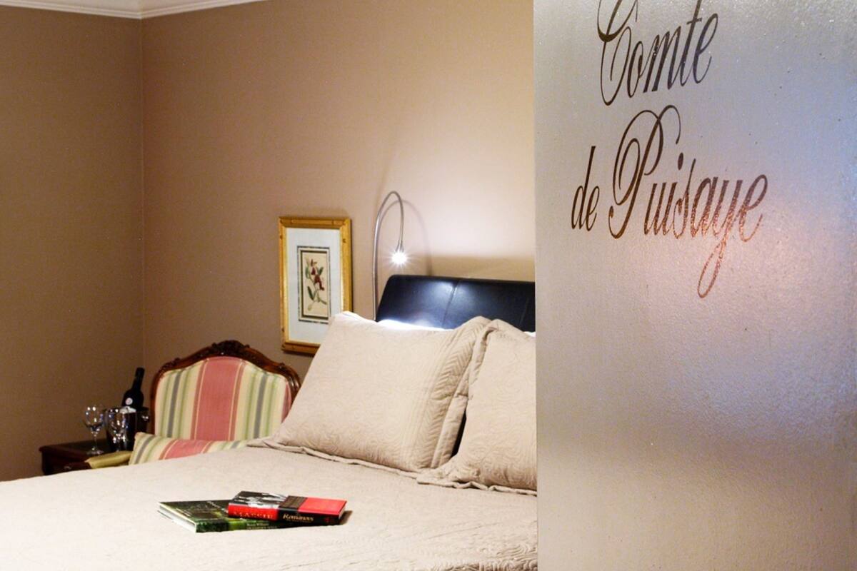 A bedroom with a bed, pillows, a bedside table with a lamp, and a framed picture on the wall.