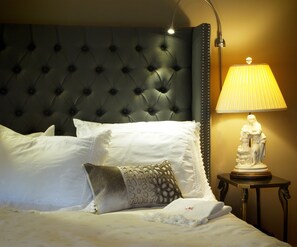 A neatly made bed with white linens and decorative pillows, a tufted headboard, a bedside lamp, and a small table with a statue. - Old Ivy Walk (Niagara-on-the-Lake)