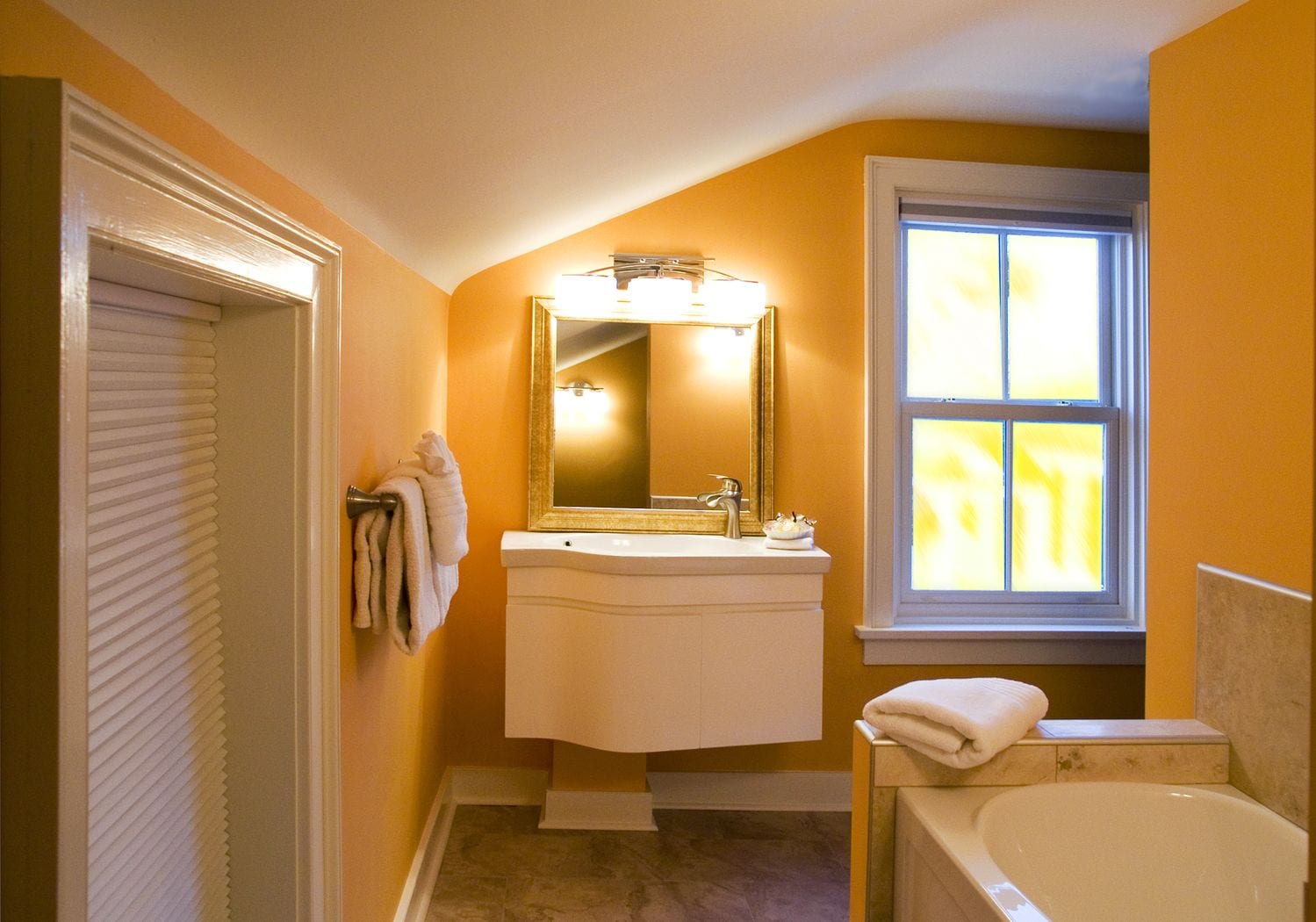 A bathroom with a white sink, mirror, and bathtub. There is a window with blinds and a towel rack with towels.