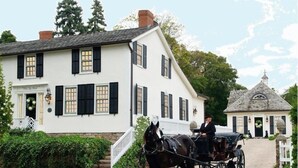 A white building with black shutters, a horse-drawn carriage, and a smaller structure with a dome roof. - Old Ivy Walk (Niagara-on-the-Lake)