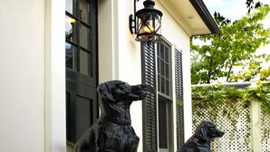 A building with two black dog statues in front, a white facade, and black shutters on the windows. - Old Ivy Walk (Niagara-on-the-Lake)