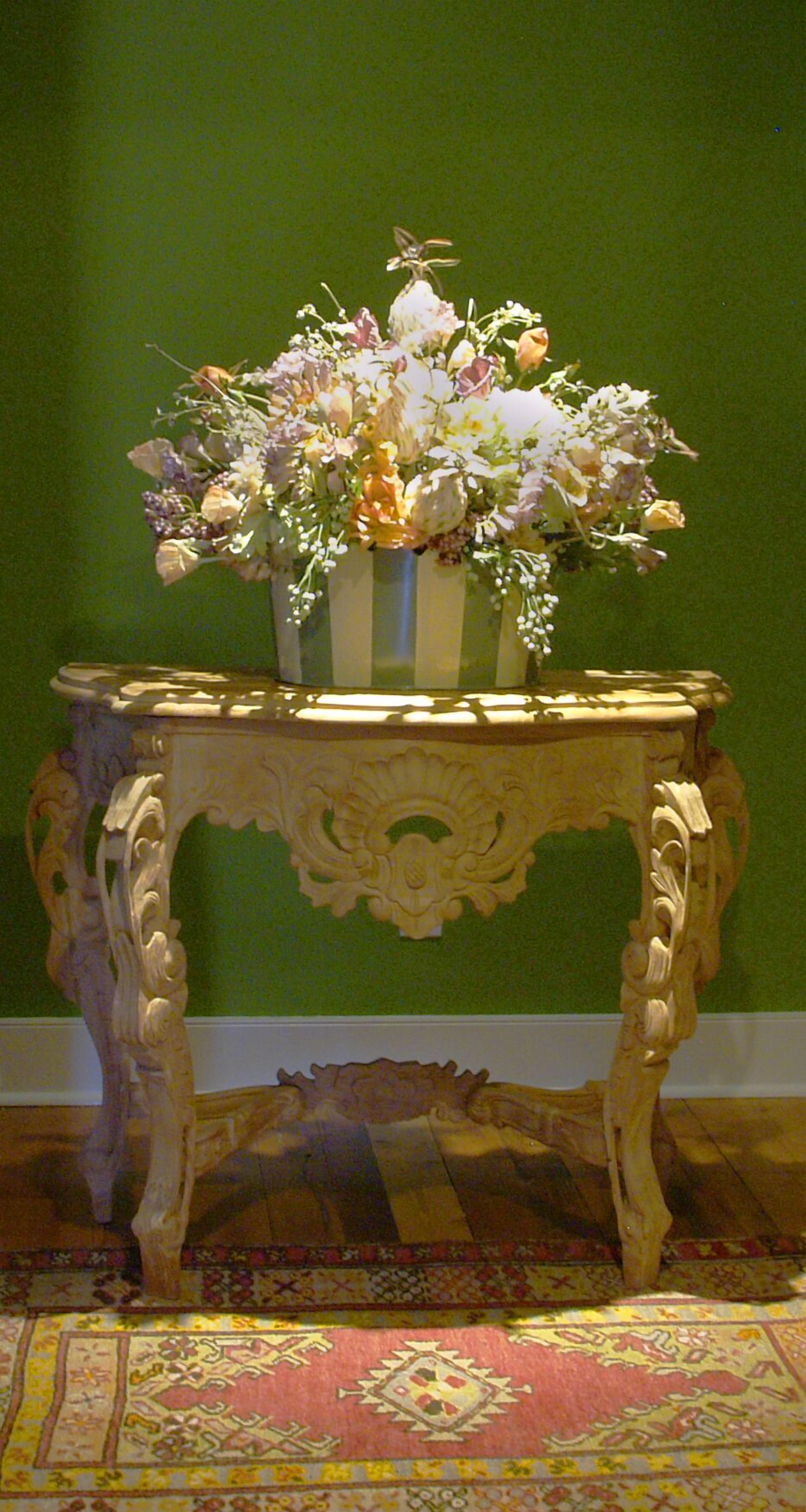 A table with a vase of flowers, ornate legs, and a patterned carpet.