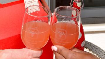 Two people holding glasses of a pink beverage, a red tray with a tag, and a bottle with a red cap.