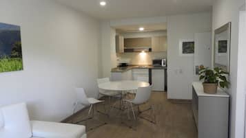 Un espace de vie moderne et compact comprenant un coin cuisine, un espace repas avec une table ronde et des chaises, et un petit coin salon avec un canapé blanc.