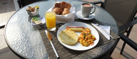 Ein runder Glastisch mit Frühstücksangeboten, darunter Croissants, ein Eierteller und ein Glas Orangensaft.
