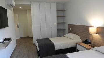 A hotel room with two beds, a wardrobe, a bedside table with a lamp, and a TV mounted on the wall.