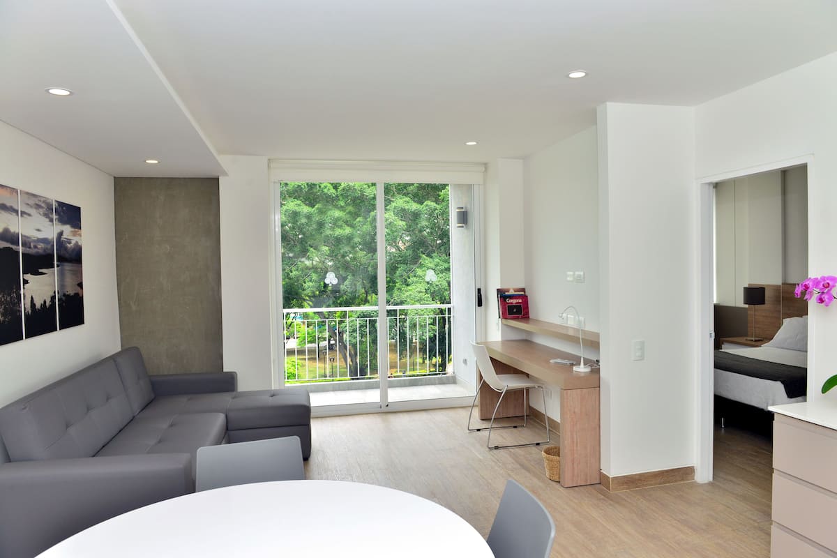 A modern living room with a gray sectional sofa, a dining table, and a kitchen area with a wooden countertop and white chairs.