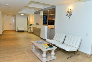Un espacio moderno con un sofá blanco, una mesa de centro con libros y un televisor montado en la pared.
