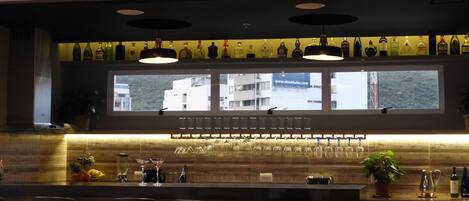 A modern bar area with a long counter, multiple bar stools, and a large window overlooking a cityscape.