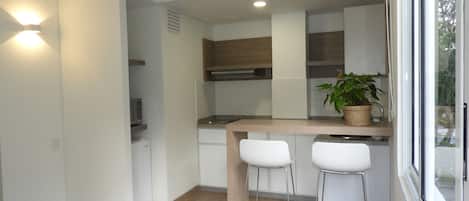 A modern kitchen with white cabinets, a wooden countertop, two white bar stools, a microwave, and a potted plant.