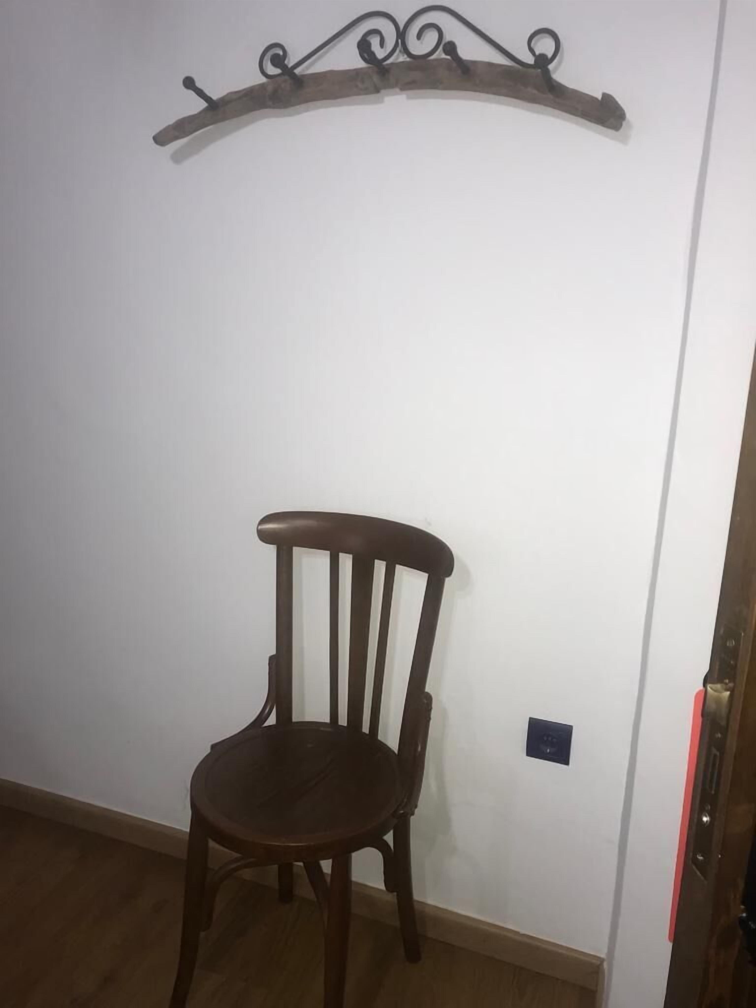 Una sedia di legno appoggiata a un muro bianco, con un elemento decorativo in metallo sopra.