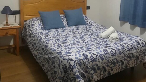 Een bed met een bloemenlaken, twee kussens en een opgerolde handdoek erop.