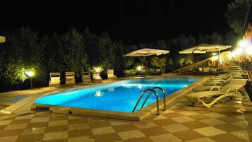 Piscina con sillones de descanso y sombrillas, rodeada de árboles y un suelo a cuadros.