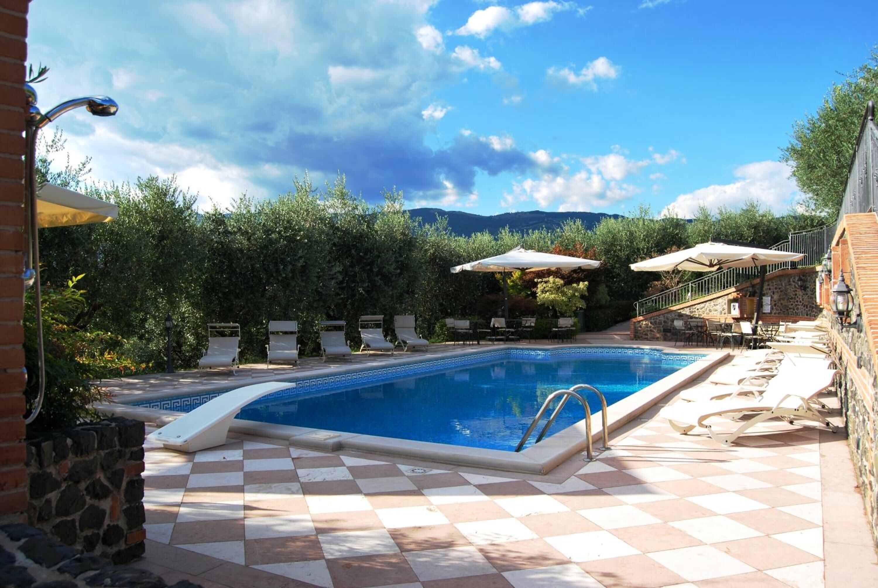 A swimming pool with checkered tiles, lounge chairs, umbrellas, and a stone wall.