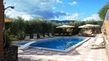 A swimming pool with checkered tiles, lounge chairs, umbrellas, and a stone wall.