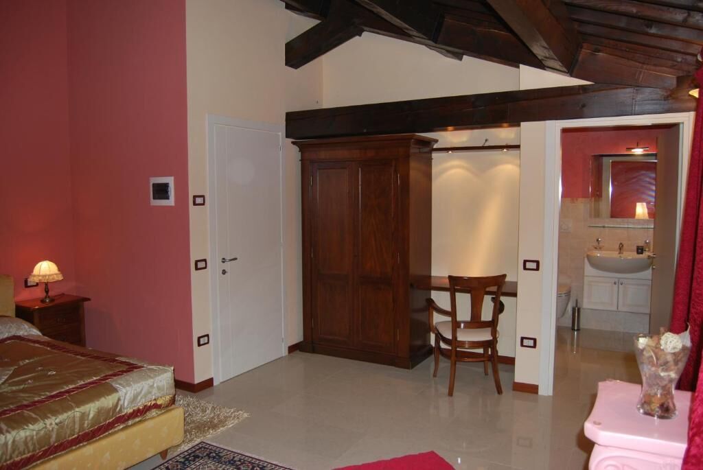 A bedroom with a bed, a wooden wardrobe, a chair, and a small table with a lamp.