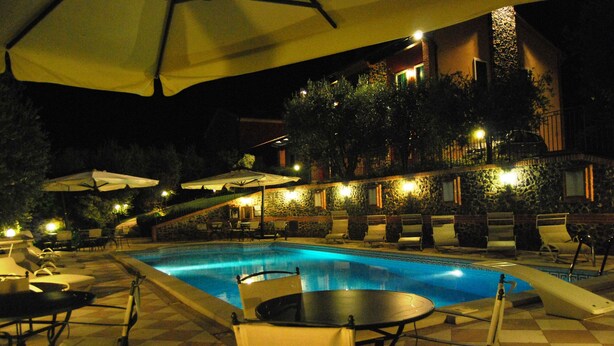 A nighttime pool area with lounge chairs, umbrellas, and a stone wall. - Tenuta Fortelongo (Fara Vicentino)