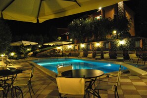 A nighttime pool area with lounge chairs, umbrellas, and a stone wall. - Tenuta Fortelongo (Fara Vicentino)