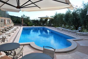 A swimming pool with lounge chairs and umbrellas, surrounded by stone walls and greenery. - Tenuta Fortelongo (Fara Vicentino)