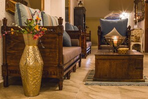 Une chambre de style traditionnel, avec un grand vase décoratif, un lit en bois doté d’une tête de lit, une table de chevet en bois et un fauteuil bleu recouvert de tissu.