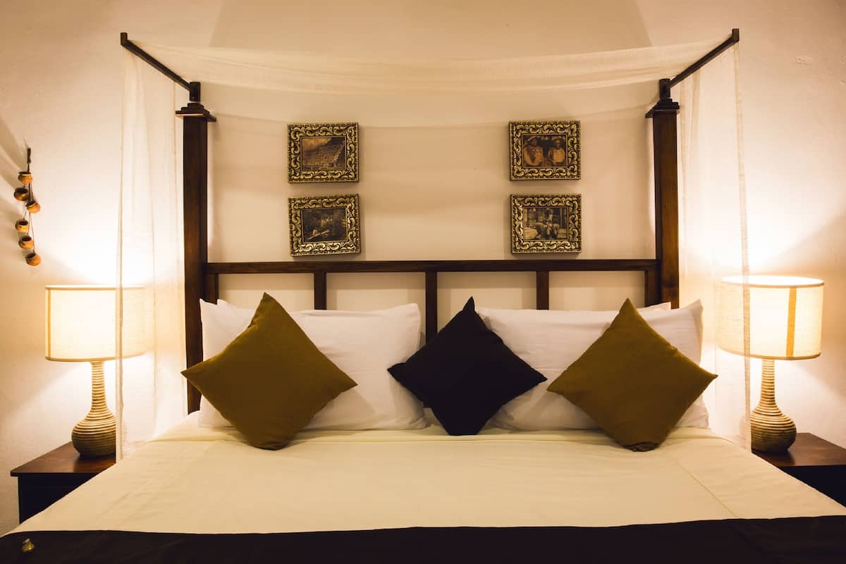 A four-poster bed with a canopy, two bedside lamps, and four framed pictures on the wall.