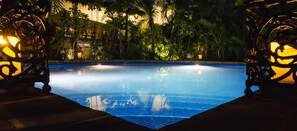 Une piscine entourée d’une végétation luxuriante et bordée de réverbères décoratifs.