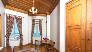 A room with a wooden ceiling, a chandelier, a dining table with chairs, a patterned rug, and a large wooden door. - Mom Hotel (Adalar)