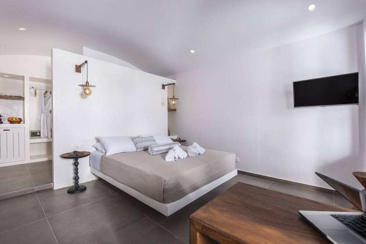 A modern bedroom with a bed, bedside tables, a TV, and a wooden desk.