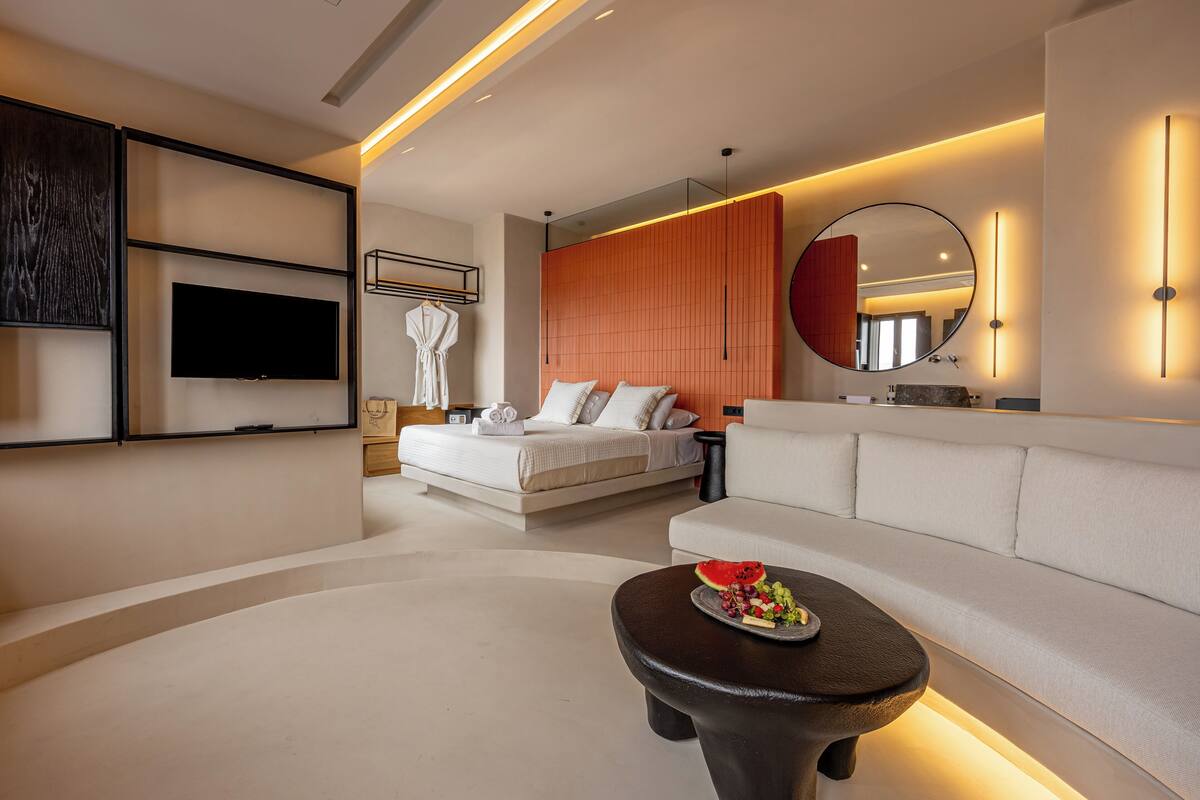 A modern hotel room with a large bed, a sofa, a TV, and a round mirror.