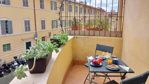 Een balkon met een ontbijtje, plantenpotten en uitzicht op omliggende gebouwen.