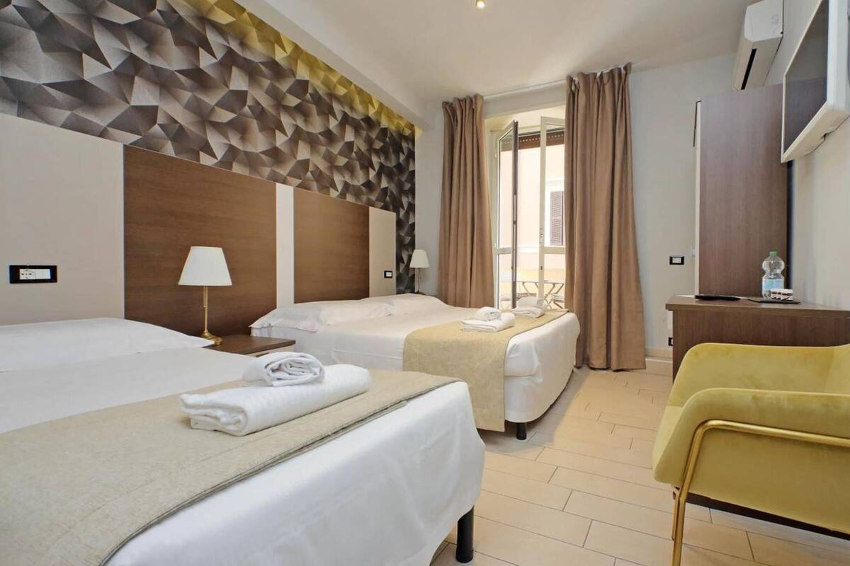 A hotel room with two beds, a desk, a chair, and a large window with curtains.
