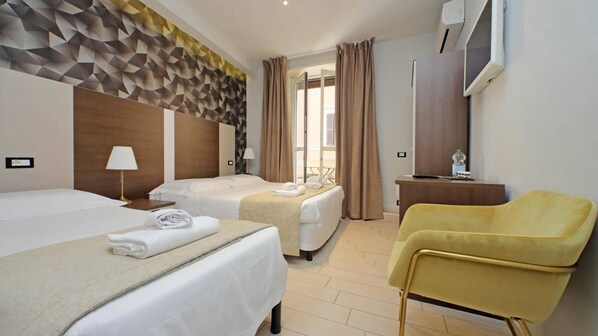 Habitación de hotel con dos camas, un escritorio, una silla y un ventanal con cortinas.