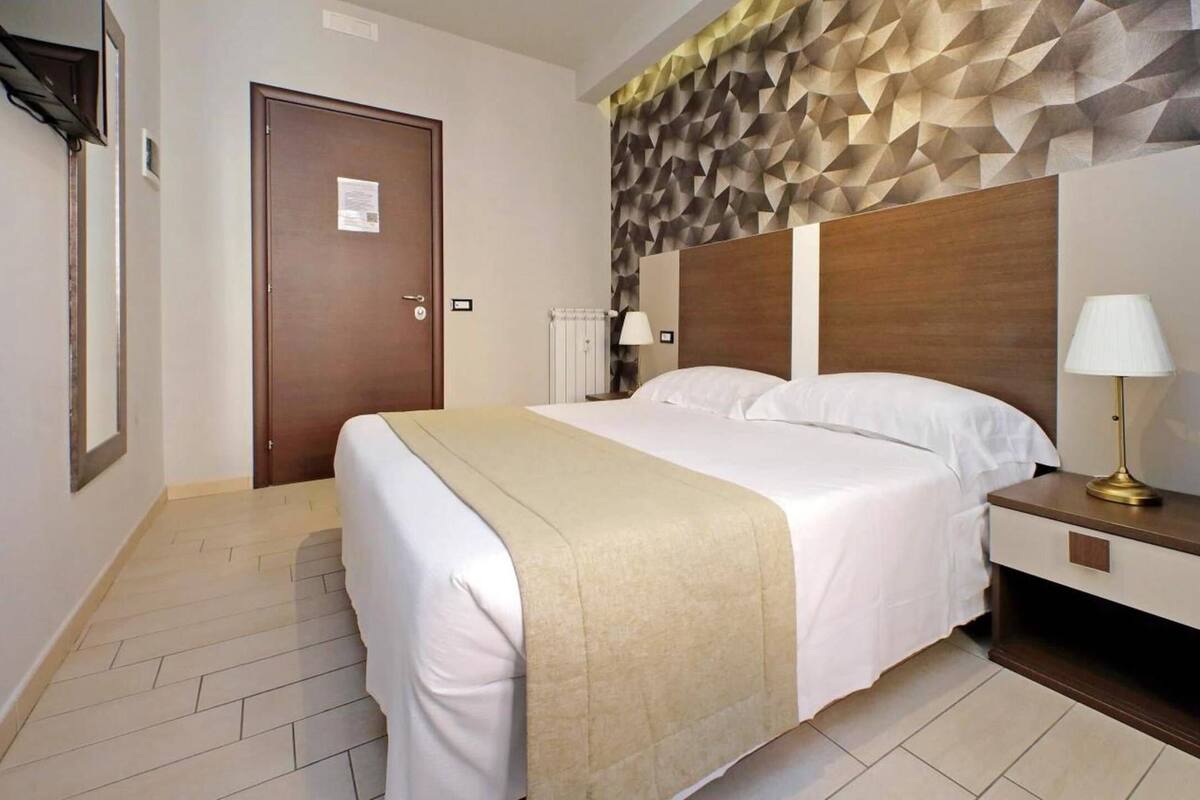 A hotel room with a bed, bedside table, lamp, and a geometric-patterned wall.