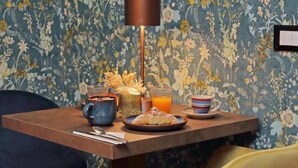 Een ontbijtje met een mok, een bord gebakjes, een glas sinaasappelsap en een kaars op een houten tafel.