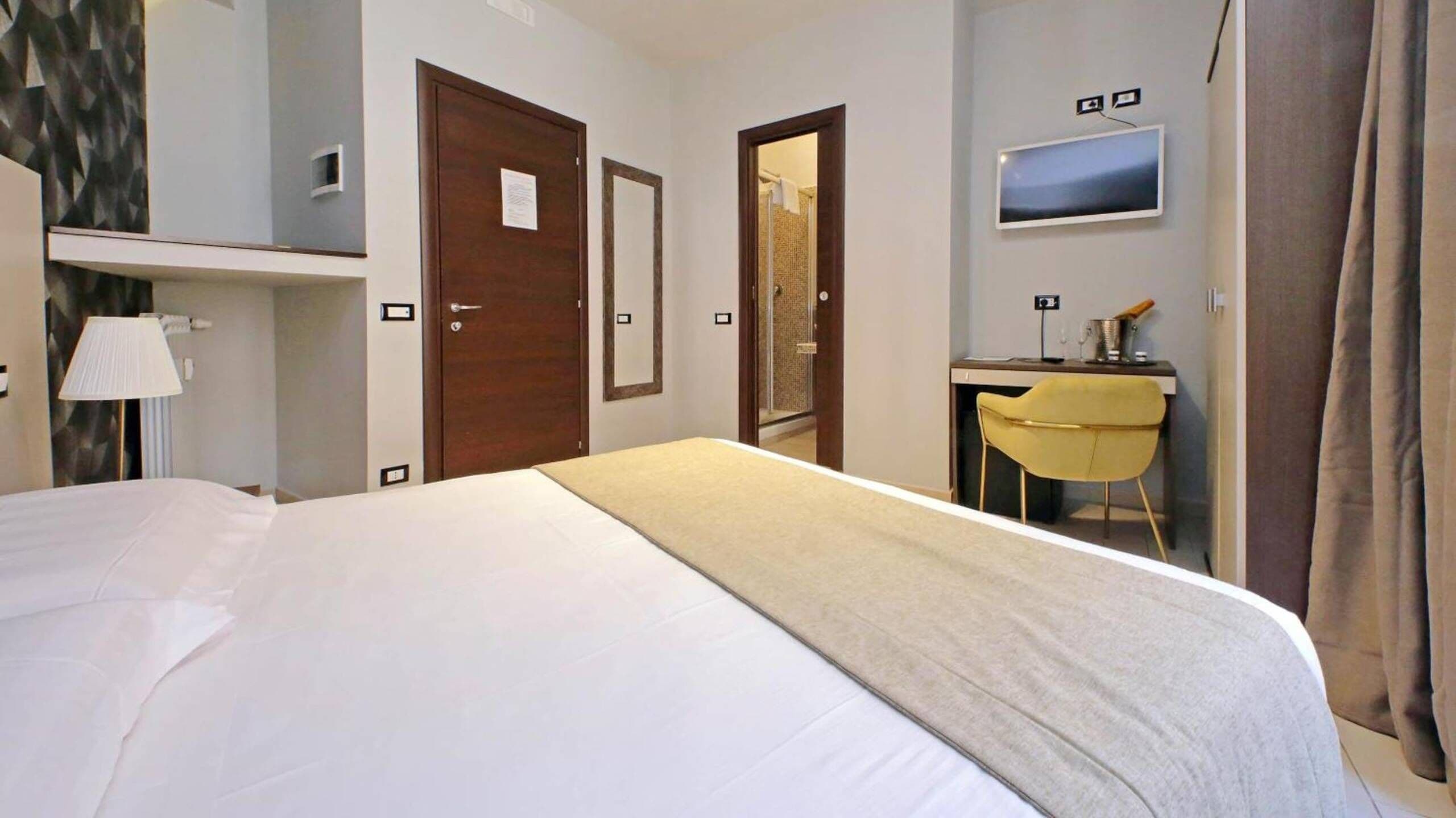 Una habitación de hotel con cama, escritorio, silla, televisión y ducha.