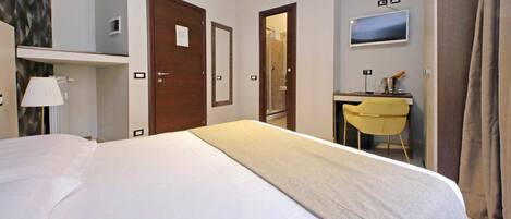 Una habitación de hotel con cama, escritorio, silla, televisión y ducha.