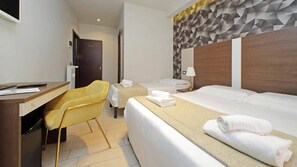 Habitación de hotel con escritorio, una silla amarilla, dos camas y un cabecero estampado con un diseño geométrico.