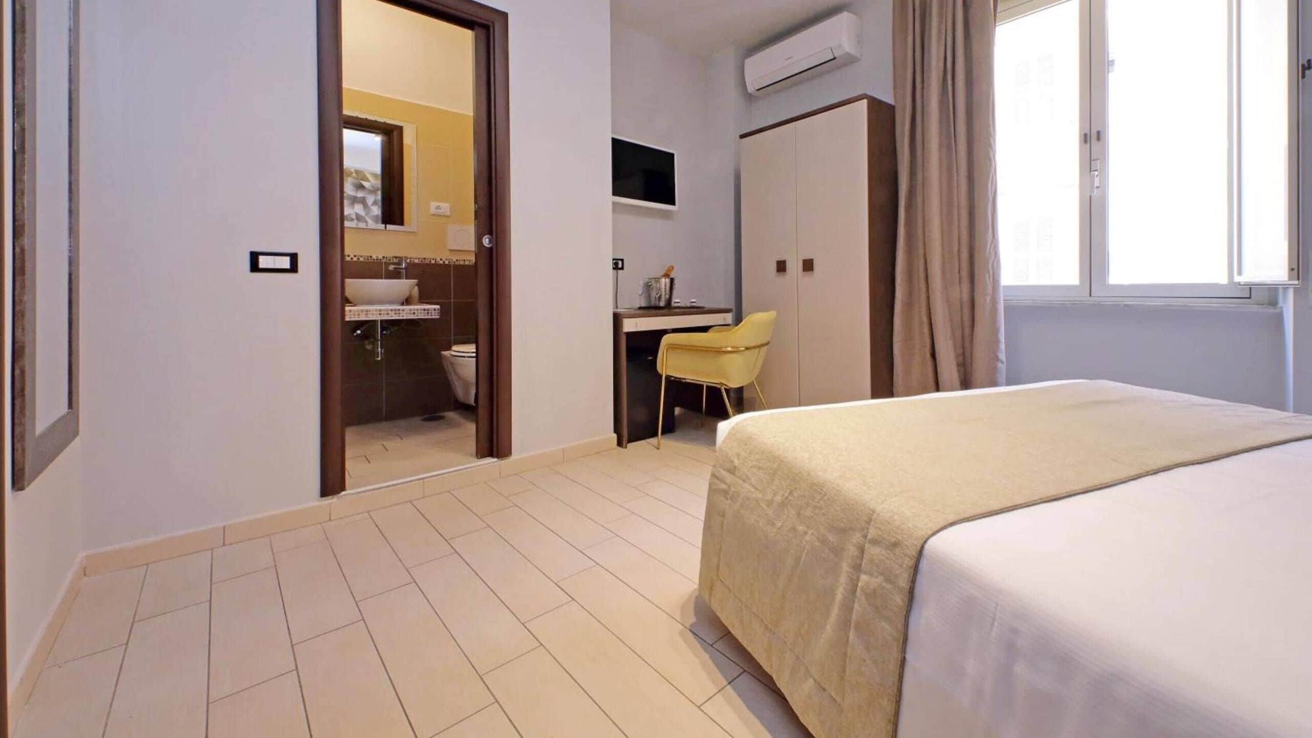 A hotel room with a bed, a desk with a chair, a bathroom, and a window with curtains.